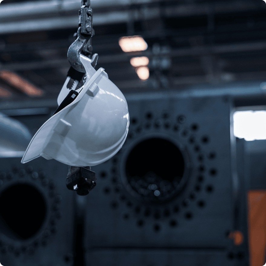 White hard hat hanging from a crane hook in a plant