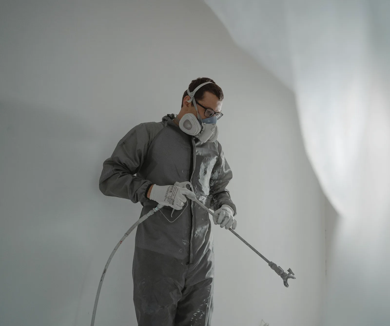 Worker in a respirator, coveralls, glasses and gloves spraying a coating