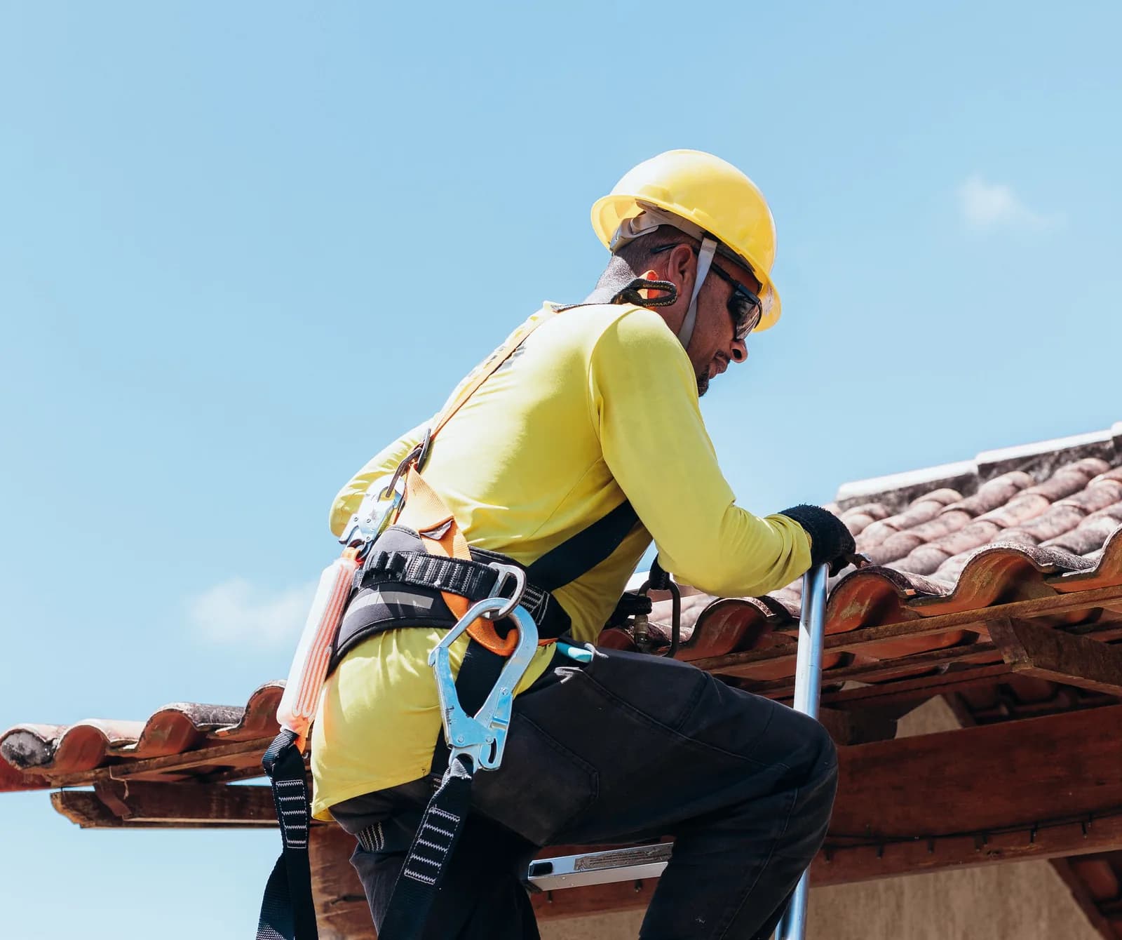 Worker in a fall-protection harness, hard hat and gloves climbing onto a roof
