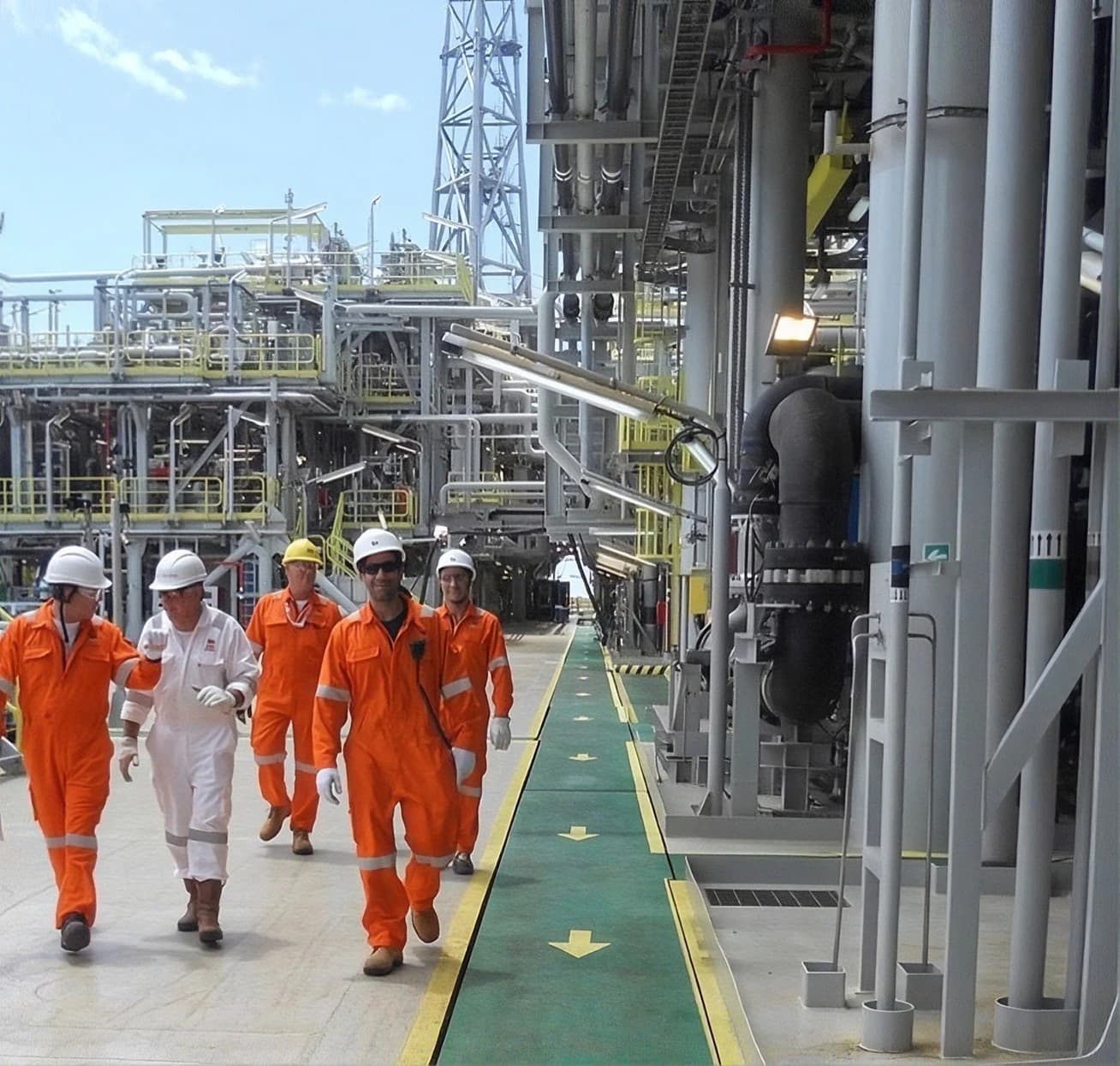 Crew in orange coveralls walking a plant walkway