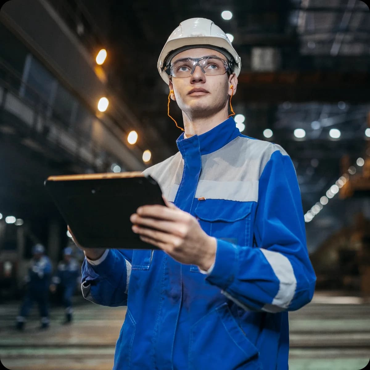 Plant worker in a hard hat and safety glasses reporting on a tablet
