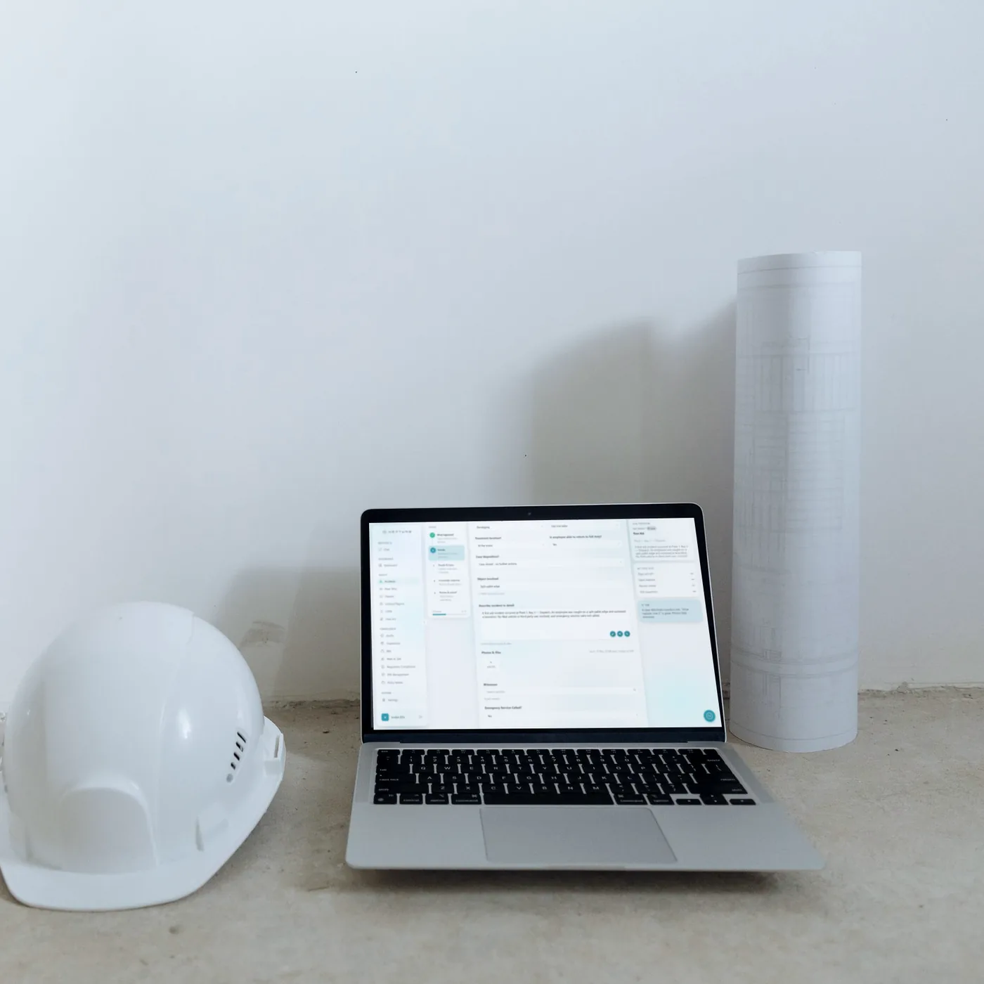 Laptop on a site floor beside a hard hat, showing an AI-drafted incident description