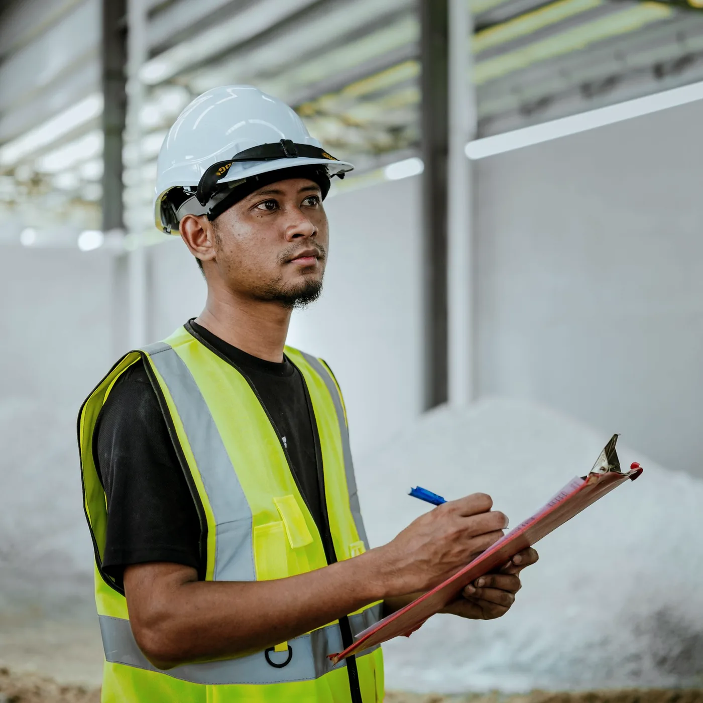 Inspector in a hard hat and hi-vis vest recording findings on a clipboard