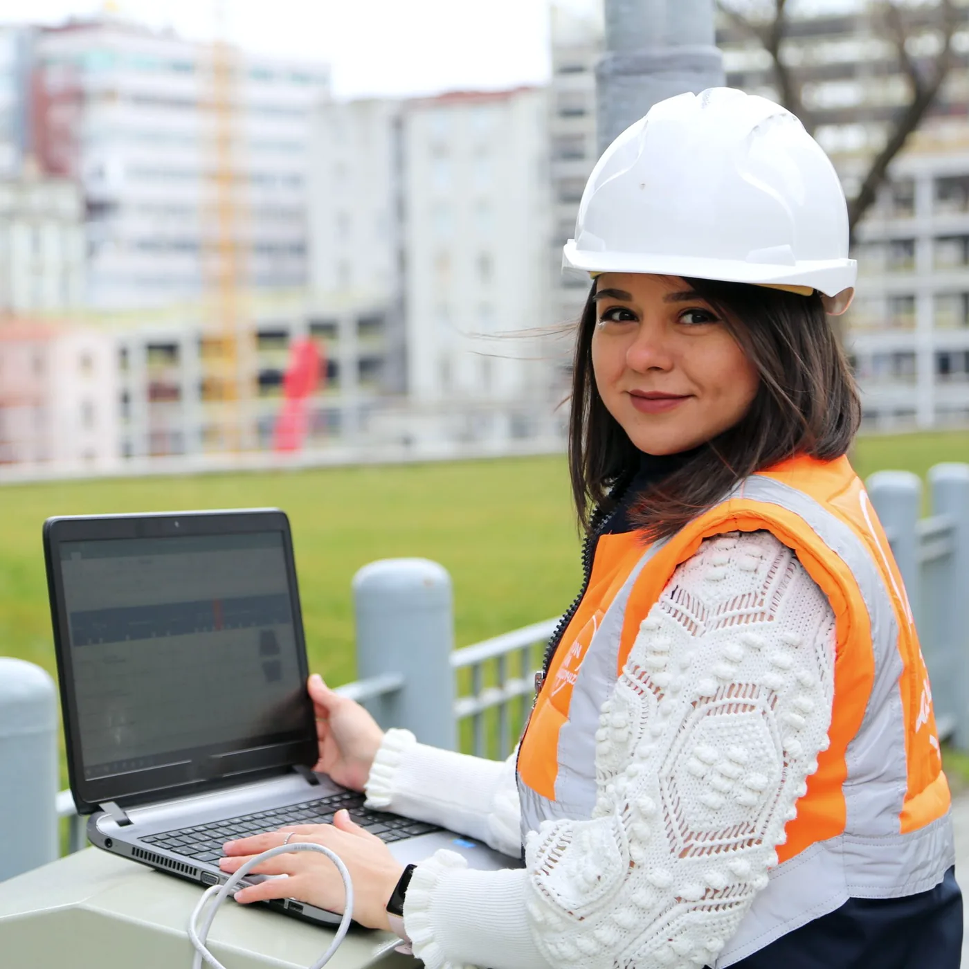 Engineer in a hard hat and hi-vis vest working on a laptop on site