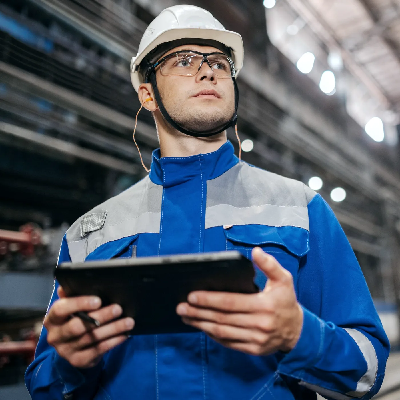 Worker in a hard hat and safety glasses holding a tablet on the plant floor
